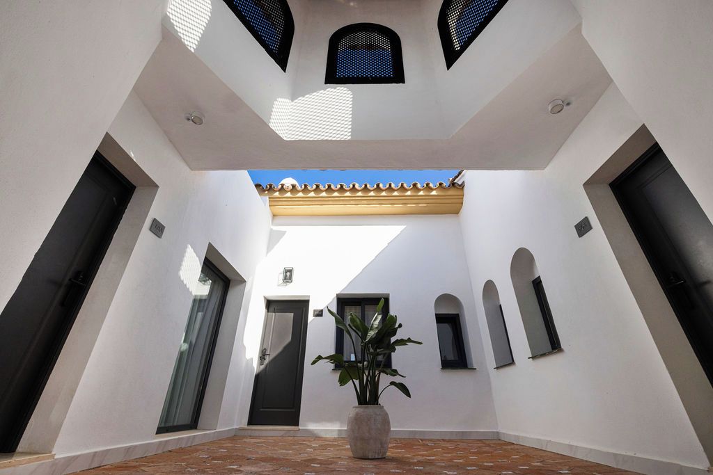 A spacious courtyard with a tiled floor, a central potted plant, and a ceiling with geometric patterns.