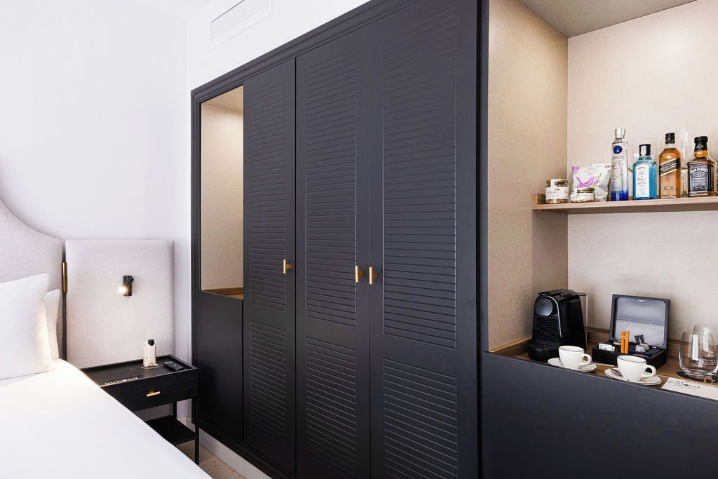 Una habitación de hotel con cama, mesita de noche, armario y estante con artículos de aseo.