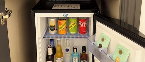 A minibar with a coffee machine, two cups, a chocolate bar, and various beverages.