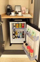 Un mini bar con una cafetera, dos tazas, una barra de chocolate y diversas bebidas.
