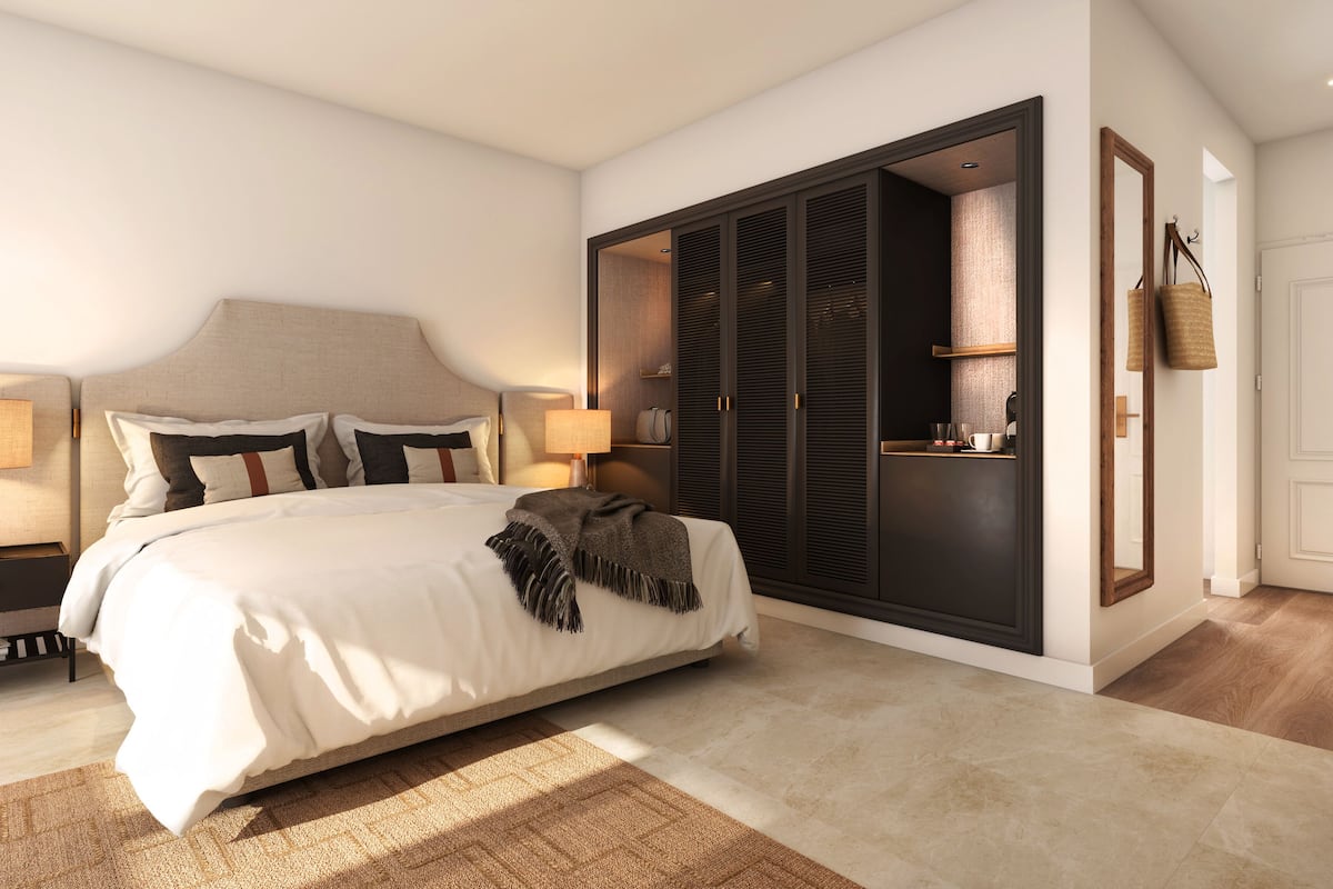 Un dormitorio moderno con una cama grande, mesitas de noche con lámparas, un armario y una pequeña zona de estar con una silla y una mesa.