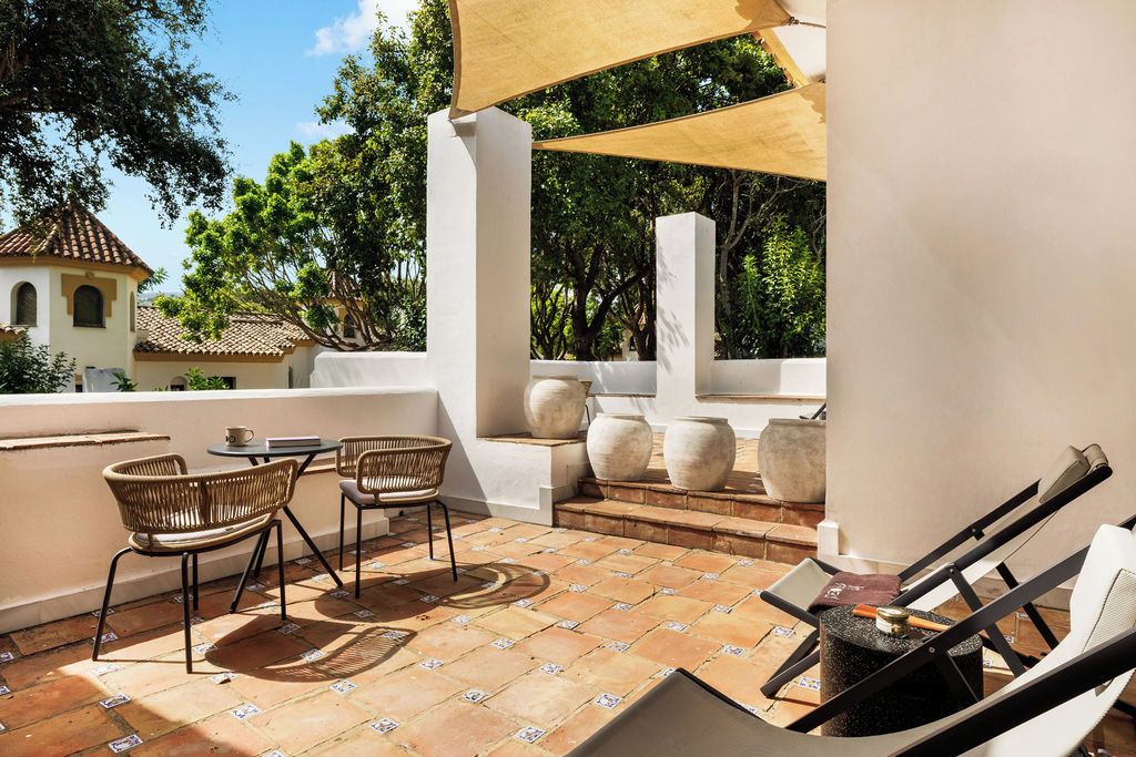 Un patio exterior con una mesa, sillas, un toldo y jarrones decorativos.