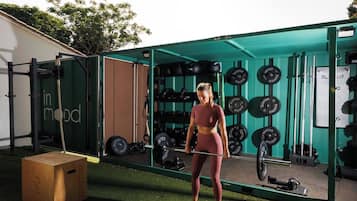 Eine Person trainiert im Freien in einem Fitnessbereich mit einer grünen Struktur, Gewichte und einer Langhantel.