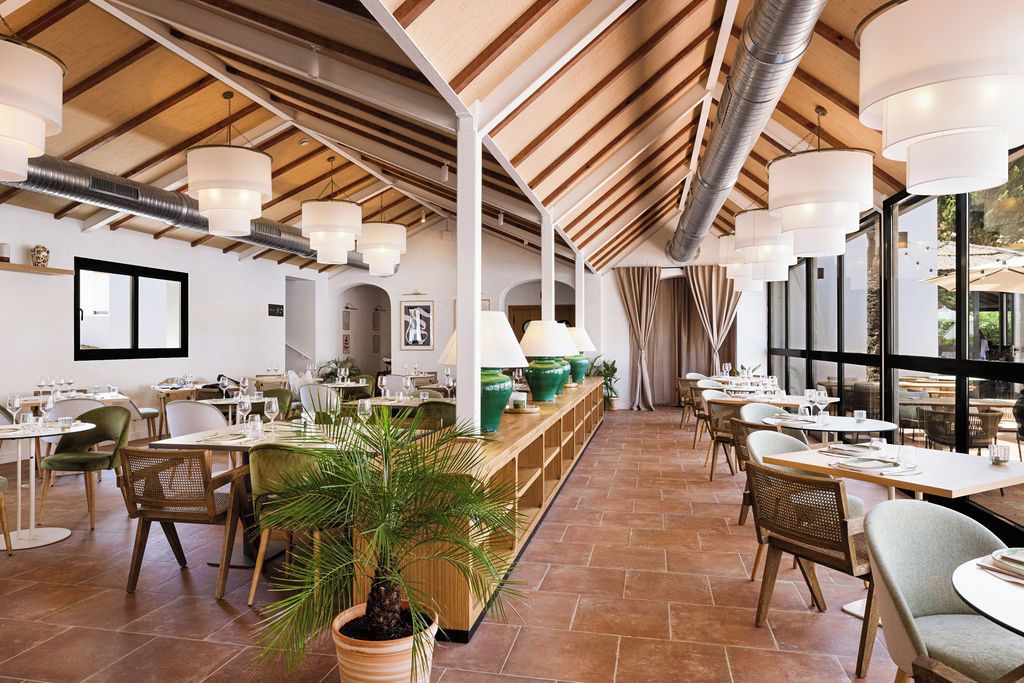 A spacious restaurant with high ceilings, wooden beams, and a long counter with seating on both sides.