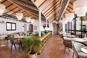 Un restaurant spacieux avec de hauts plafonds, des poutres en bois et un long comptoir avec des sièges de chaque côté.