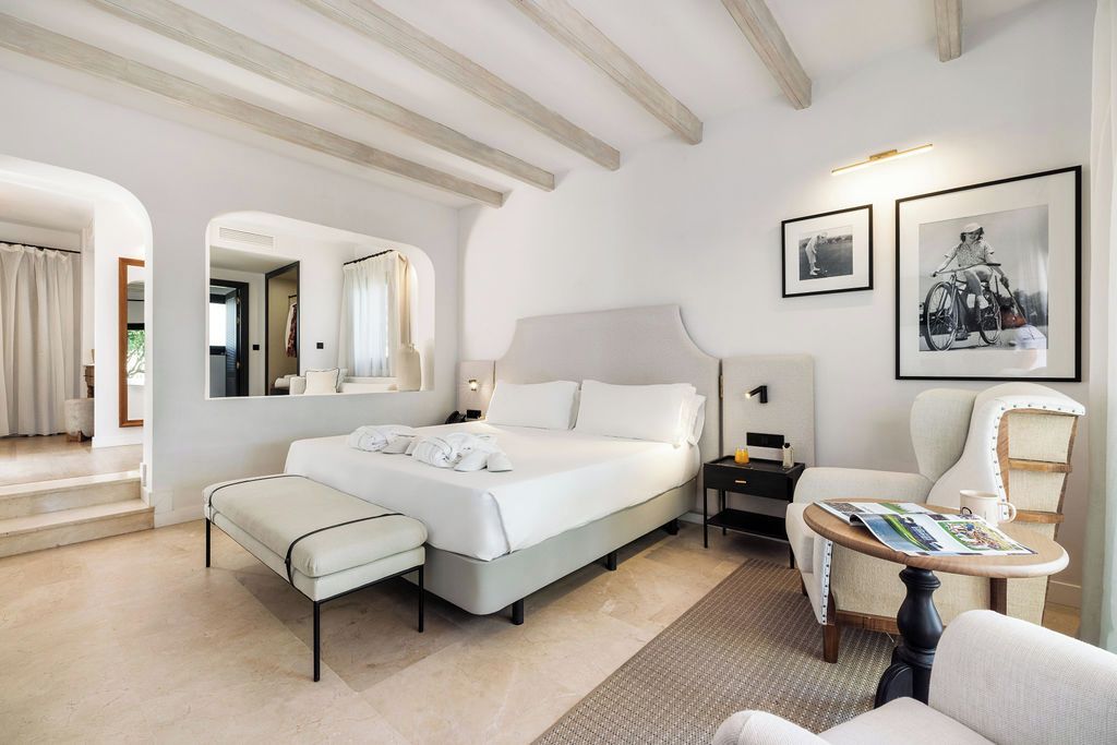 A hotel room with a large bed, a sitting area with a table, a chair, and a small side table.