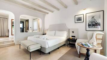 A hotel room with a large bed, a sitting area with a table, a chair, and a small side table.