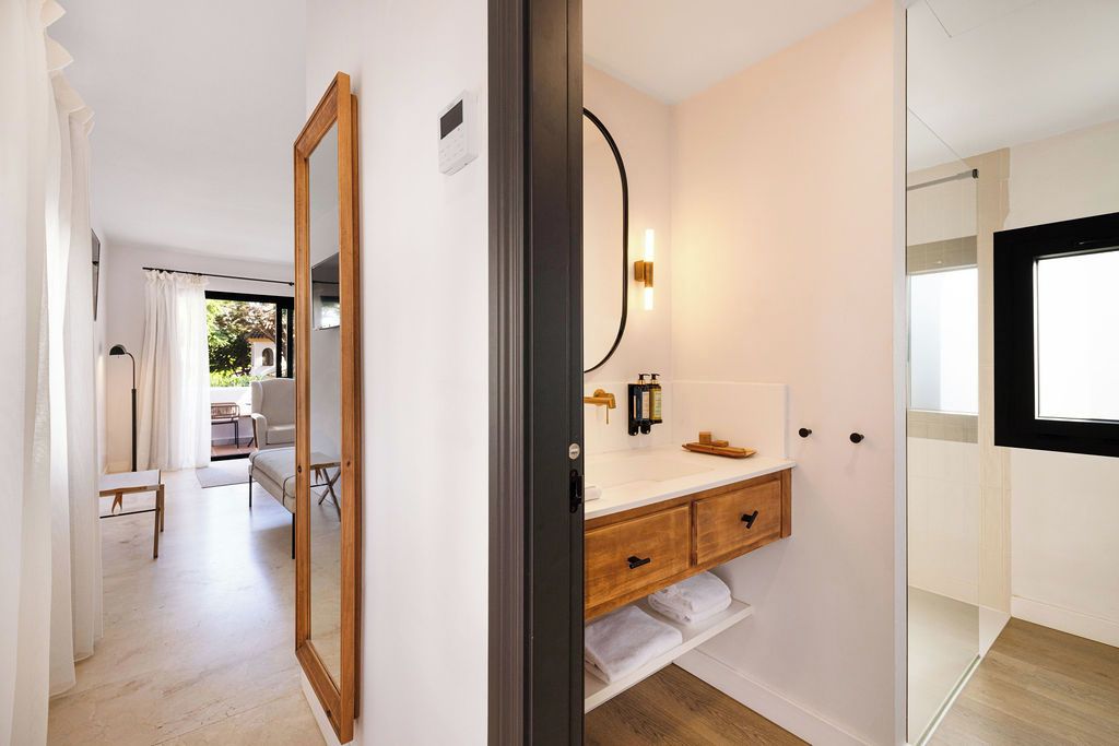 A modern bathroom with a wooden vanity, a large mirror, and a wall-mounted light fixture.