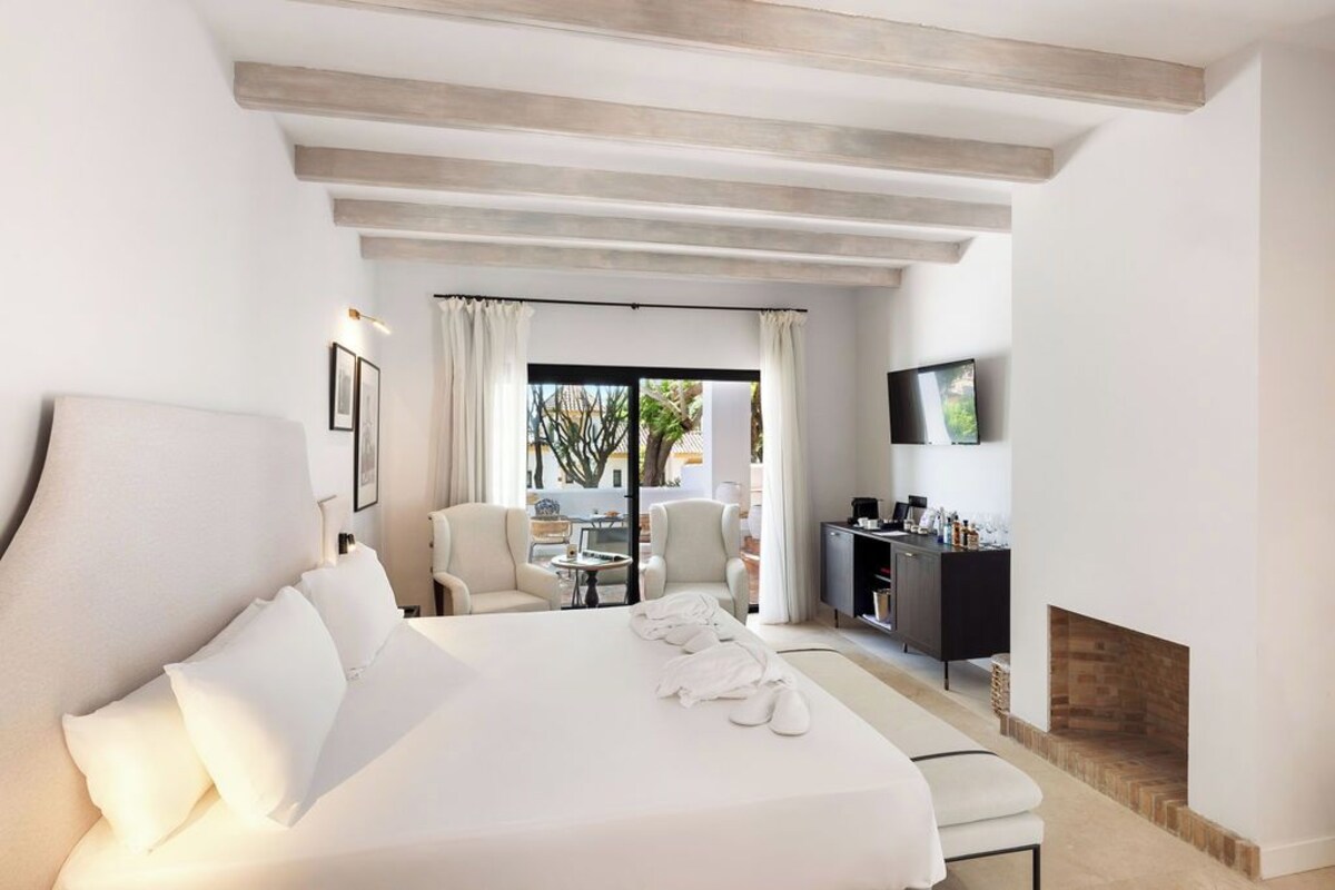 Ein Hotelzimmer mit einem großen Bett, einem Schreibtisch mit Flachbildfernseher, einem Kamin und Blick ins Freie durch eine Glastür.