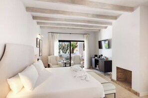 Une chambre d’hôtel dotée d’un grand lit, d’un bureau avec un téléviseur à écran plat, d’une cheminée et offrant une vue sur l’extérieur grâce à une porte vitrée.