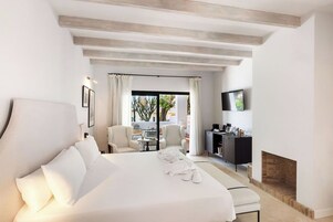 Quarto de hotel com uma cama grande, uma escrivaninha com televisão de tela plana, lareira e vista para o exterior por uma porta de vidro.