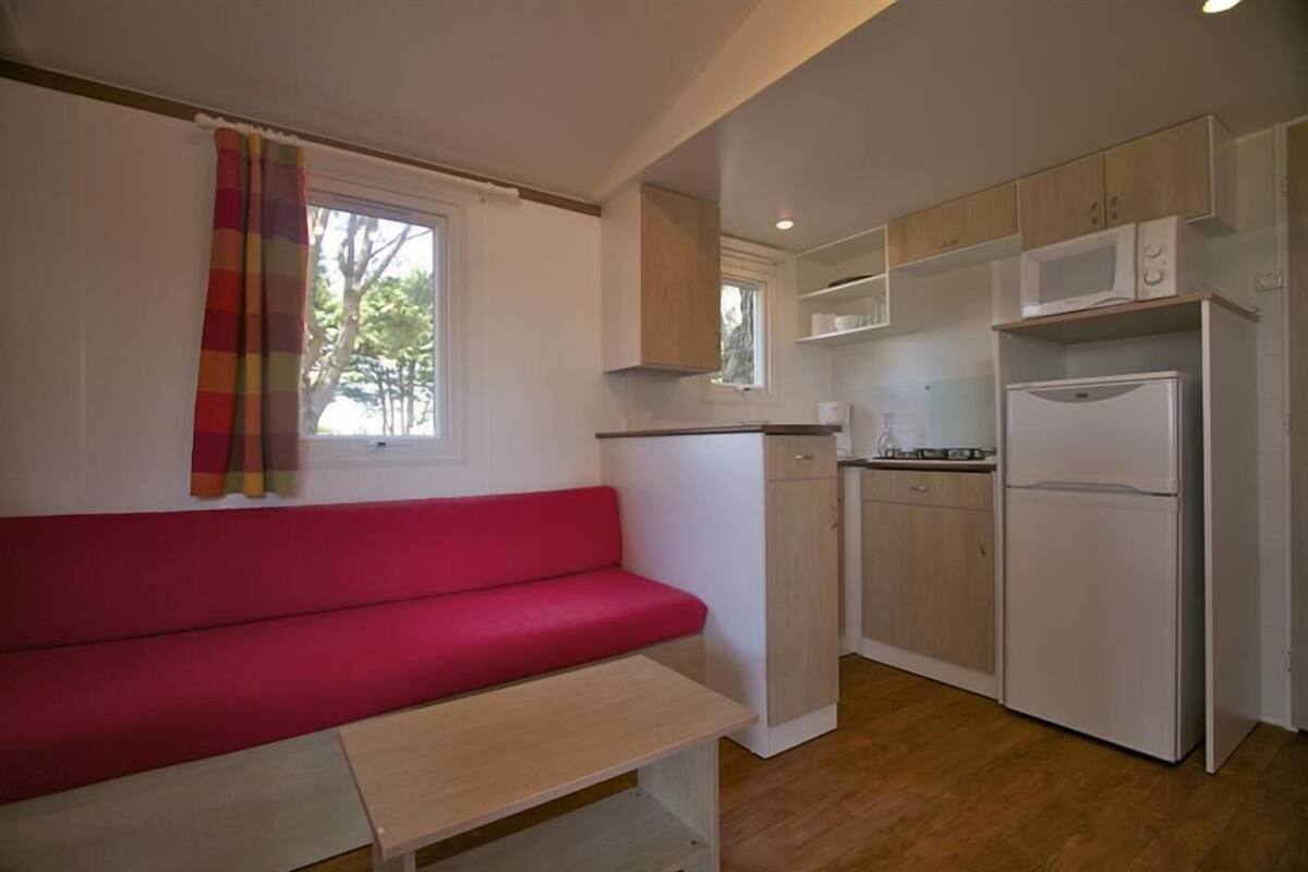 A compact kitchen with a red sofa, wooden cabinets, a microwave, and a refrigerator.
