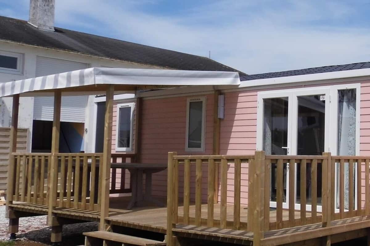 A pink mobile home with a wooden deck and a covered porch.