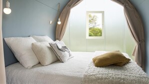 A bedroom with a sloped ceiling, a bed with white bedding, a window with curtains, and a light fixture.