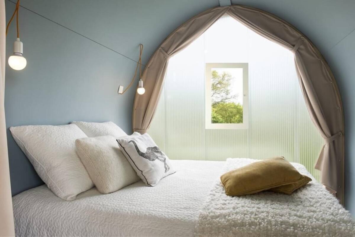 A bedroom with a sloped ceiling, a bed with white bedding, a window with curtains, and a light fixture.