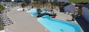 Un espace piscine comprenant plusieurs piscines, des chaises longues et des plantes en pot.