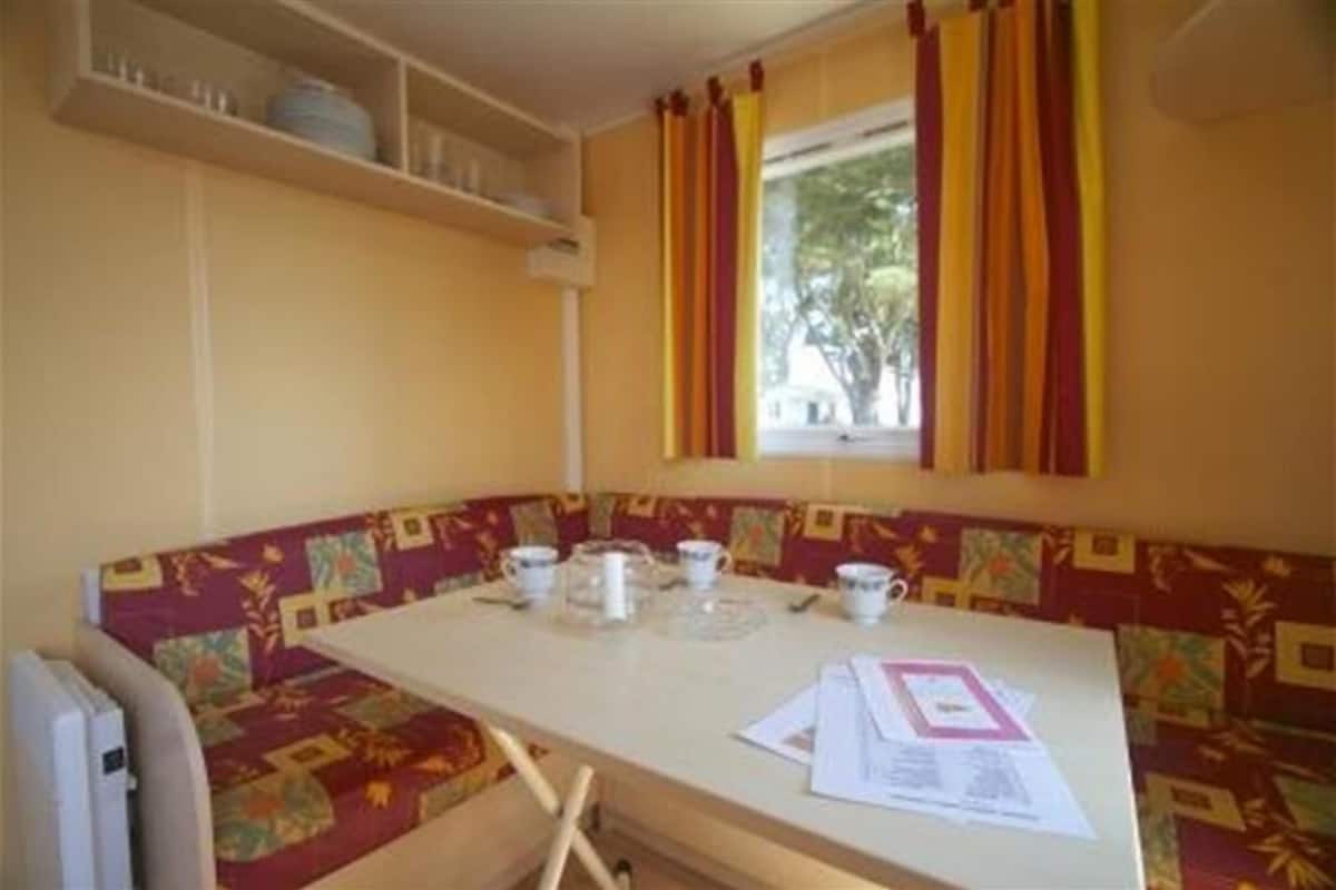 A small dining area with a table set for two, a bench with a patterned cushion, and a window with curtains.