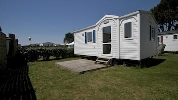 A white mobile home with a small porch and a ramp, surrounded by grass and trees.