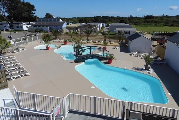 Un espace piscine comprenant plusieurs piscines, des chaises longues et des plantes en pot.