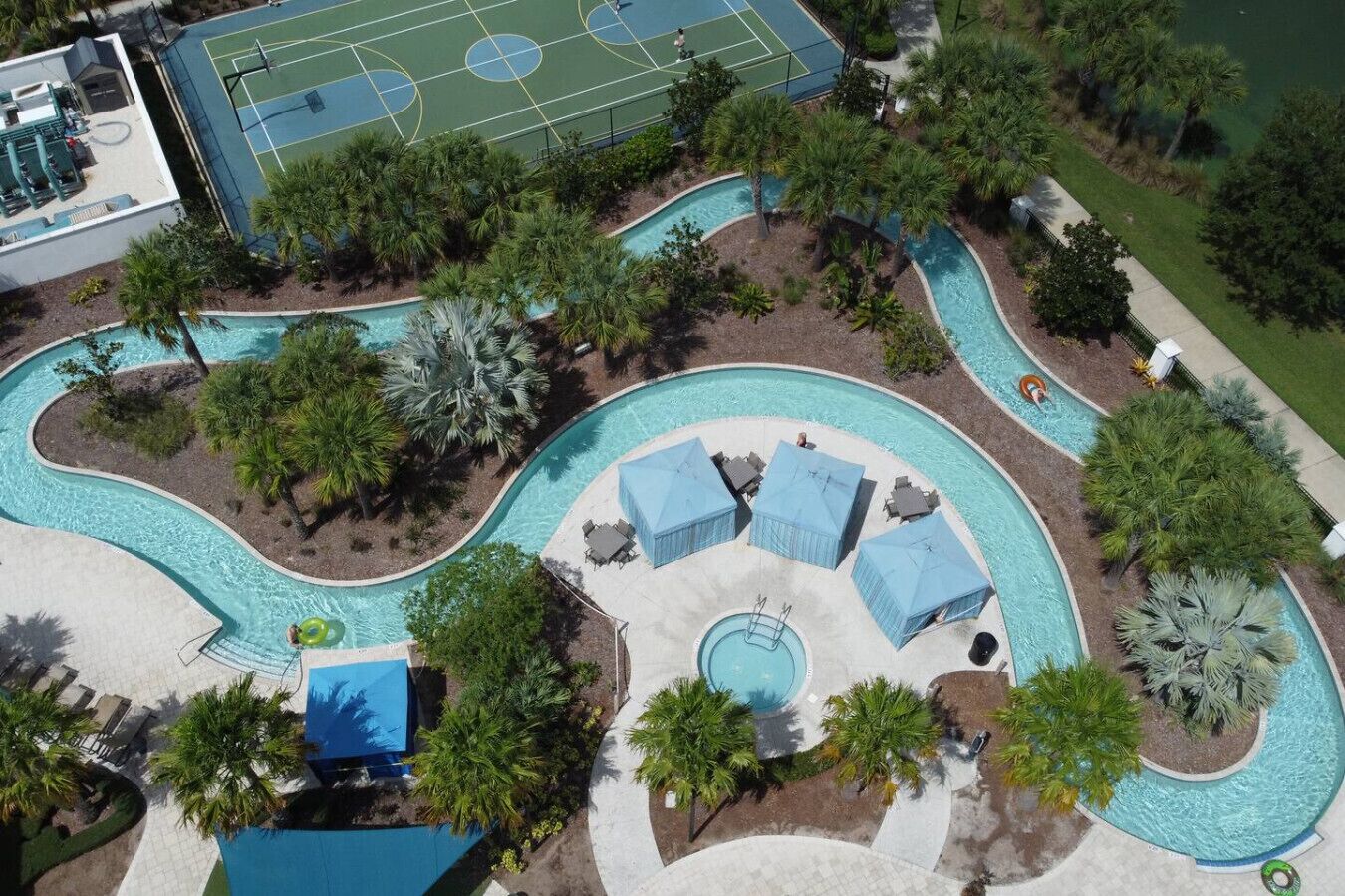 An aerial view of a resort with a swimming pool, tennis courts, and palm trees.