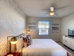 Quarto com cama grande, ventoinha no teto, televisão e janela com persianas.