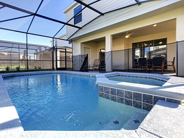 Piscina com hidromassagem, rodeada por um espaço coberto com cadeiras e uma mesa.