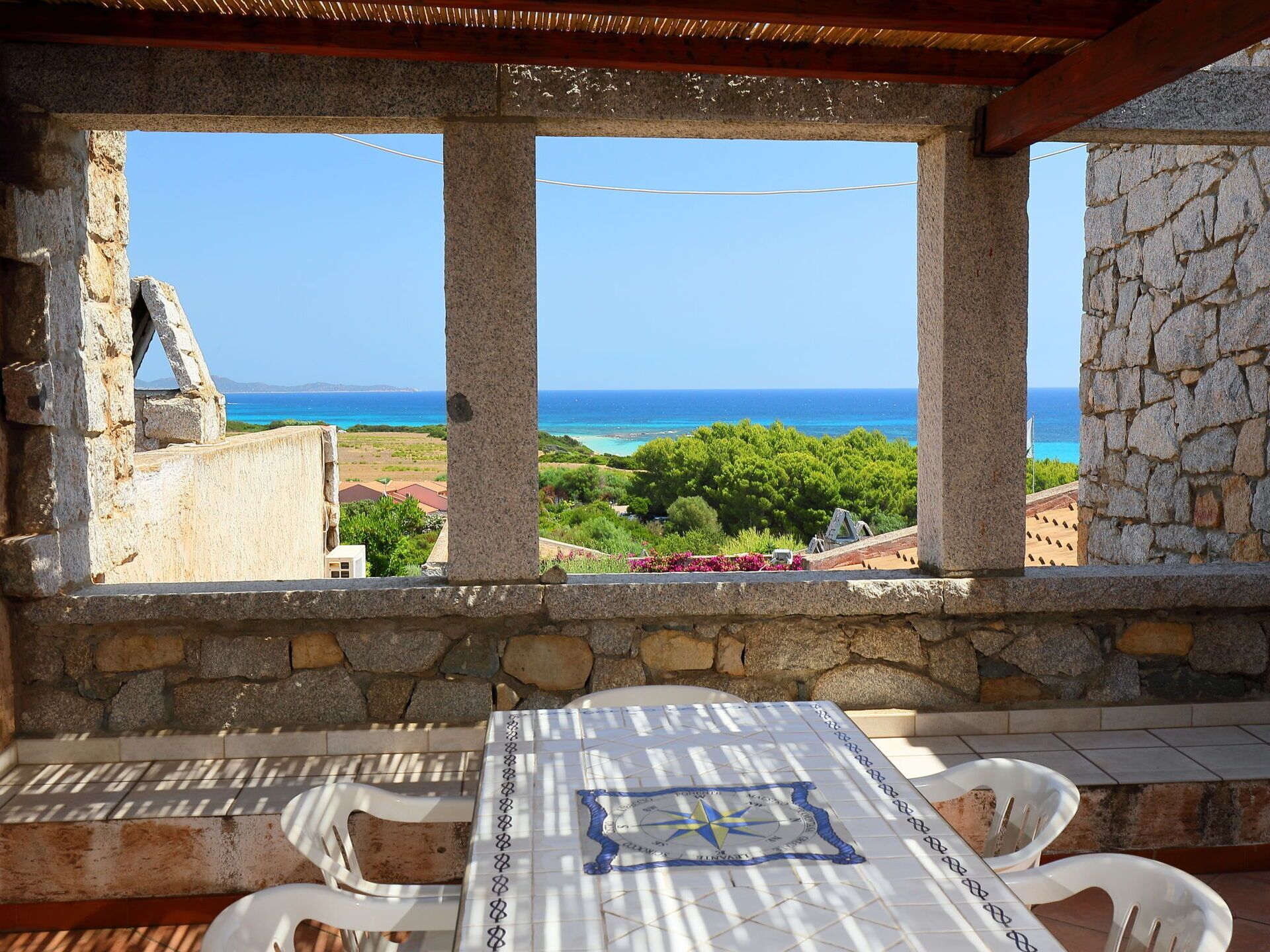 A stone-framed balcony with a view of the sea and greenery.