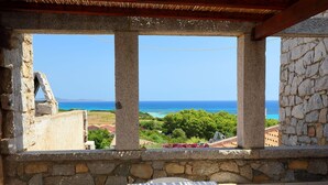 A stone-framed balcony with a view of the sea and greenery.