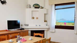 A dining area with a wooden table, chairs, a television, and a window with a view of the sea.