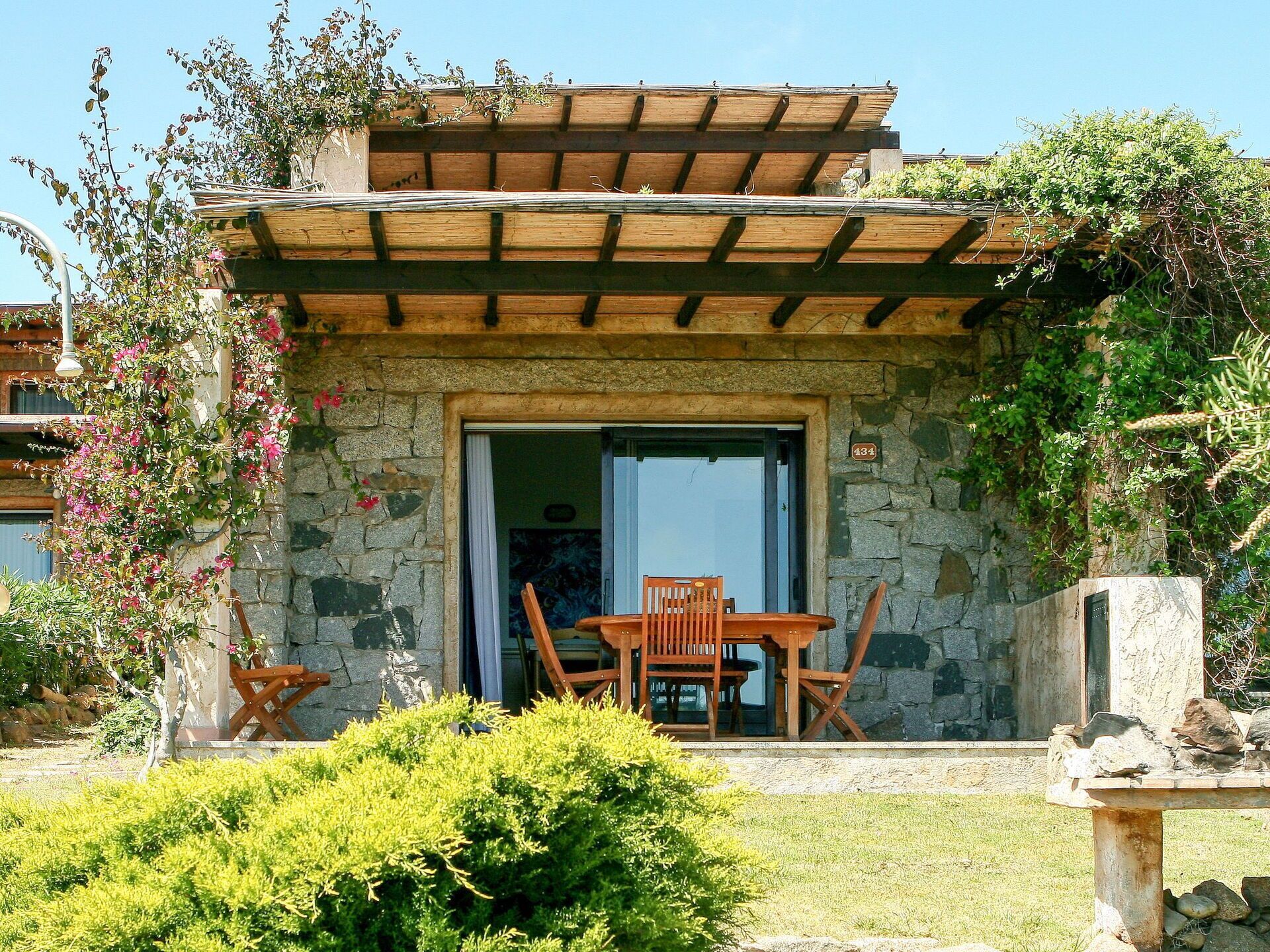 Ein Steinhaus mit einer Holzpergola, einem Tisch und Stühlen draußen sowie einer Steinsitzbank.