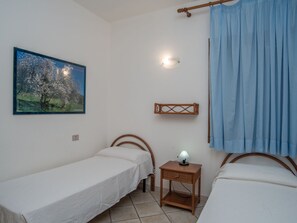 A bedroom with two single beds, a nightstand with a lamp, a wall-mounted shelf, a painting of a tree, and a window with a curtain. - Beautiful apartment in villa for 6 guests with A/C, TV, terrace and pets allowed (Sant'elmo)