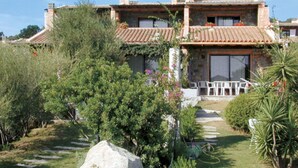 A two-story house with a tiled roof, surrounded by lush greenery and a stone pathway leading to the entrance. - Lovely apartment in villa for 6 people with A/C, TV, terrace and pets allowed (Sant'elmo)