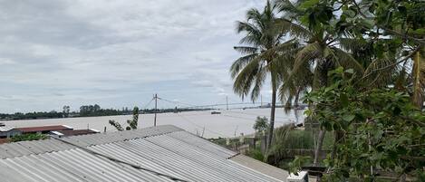 A view of a river with a bridge in the distance, surrounded by greenery and buildings with corrugated metal roofs.