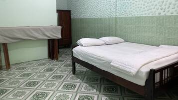 A small, clean room with a single bed, a wooden wardrobe, and a tiled floor.