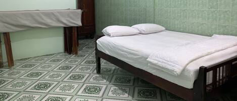 A small, clean room with a single bed, a wooden wardrobe, and a tiled floor.