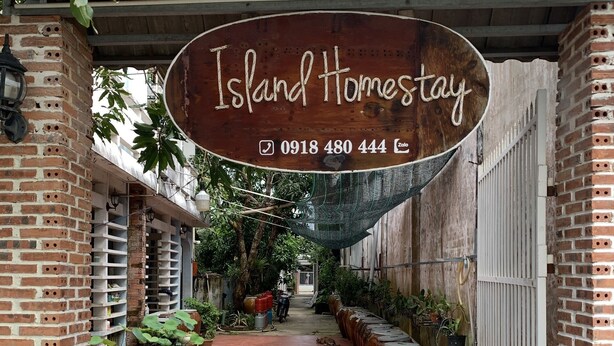En innergård med en skylt som visar ”Island Homestay” och ett telefonnummer för kontakt.
