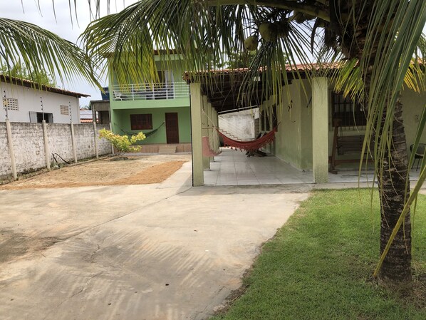 Un bâtiment à deux étages, avec une façade verte, une terrasse en béton et un hamac.