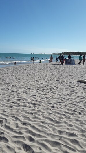 Uma praia de areia com pessoas nadando e caminhando.