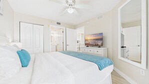 A bedroom with a bed, a TV, a ceiling fan, and a large mirror. - Coastal Elegance Upscale Renovations Ultimate Vacation Experience Surf Beach 505 (Treasure Island)