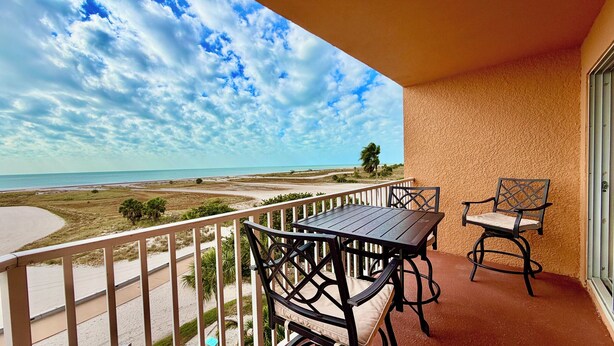 A balcony with a table and chairs, overlooking a beach and ocean. - Coastal Elegance Upscale Renovations Ultimate Vacation Experience Surf Beach 505 (Treasure Island)