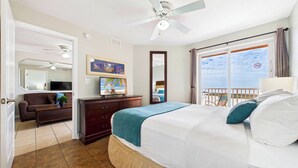A hotel room with a bed, a dresser, a television, a ceiling fan, a balcony with a view, and a door leading to another room. - Surf Beach 503 - Spectacular Sunsets - Beach Front (Treasure Island)