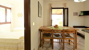 A room with a bed, a dining table with chairs, a TV, and a window with curtains.
