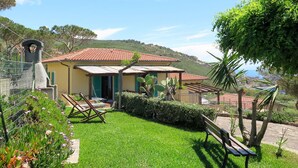 A house with a red-tiled roof, a small patio with a bench, and a garden with various plants.