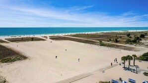 A wide sandy beach with a clear view of the ocean, a few people walking, and a few beach umbrellas. - Surf Beach 604 - Spectacular Sunsets - Beach Front (Treasure Island)