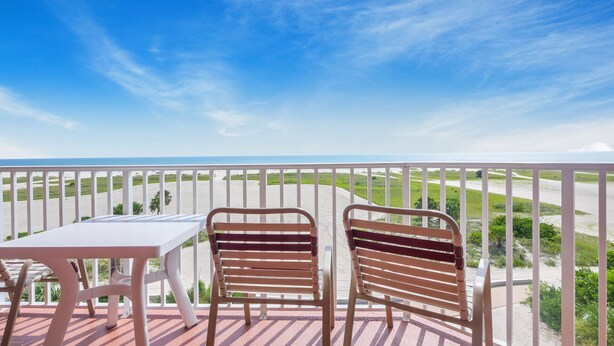 A balcony with two wooden chairs and a table, overlooking a beach and ocean. - Surf Beach 604 - Spectacular Sunsets - Beach Front (Treasure Island)