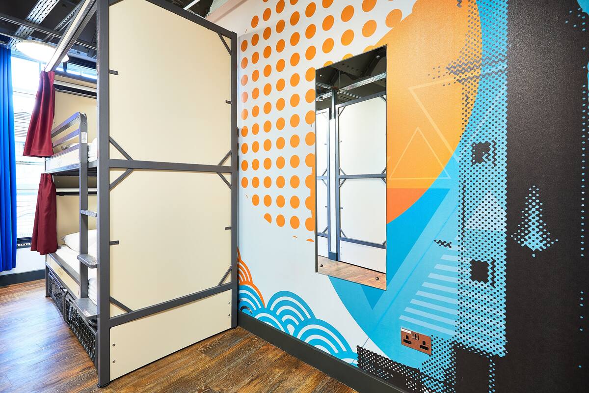 Una habitación con una cama litera, una ventana con cortinas y una pared con un diseño geométrico.