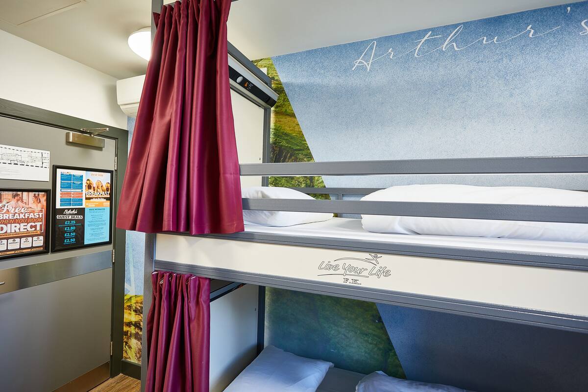 Una cama individual doble con un letrero que dice "Live Your Life", una ventana con cortinas, y una pared con una vista parcial de un cartel.
