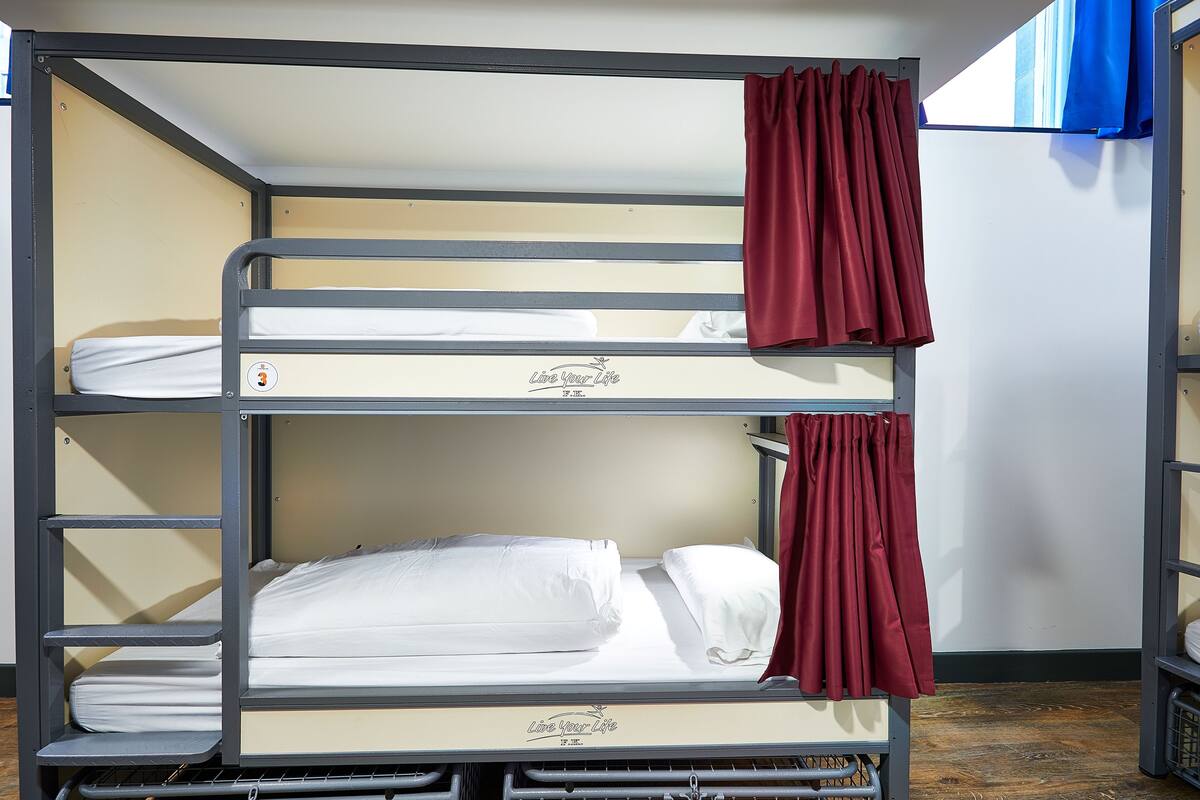 Una cama litera con tres niveles, cada uno con un colchón blanco y una cortina roja.