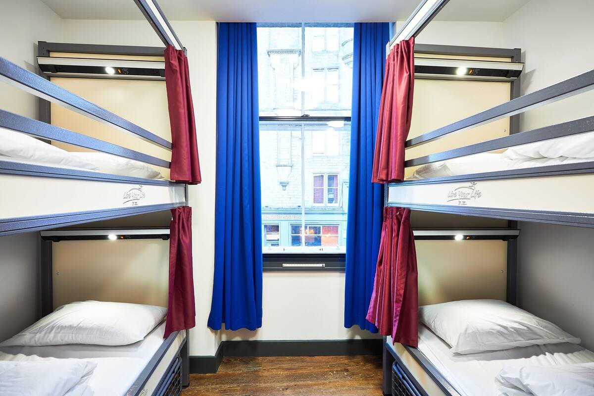 Dormitorio con literas, cortinas azules y ventana con vista a edificios.