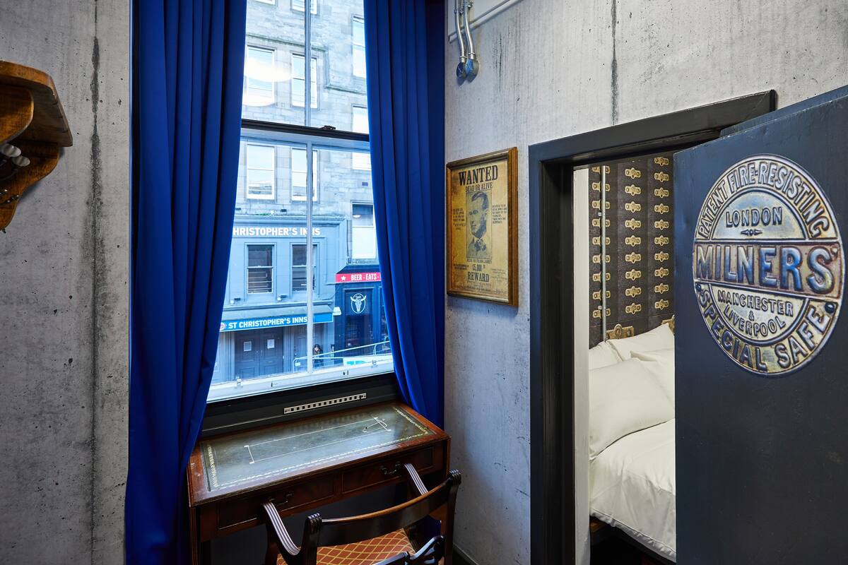 Una habitación con ventana, un escritorio de madera, una cama y una pared con un emblema de seguridad contra incendios.